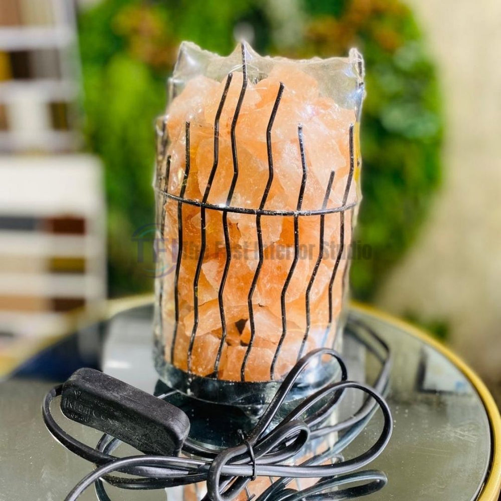 A Himalayan salt lamp featuring a hand-carved salt bowl filled with glowing pink salt spheres, resting on a crossed wooden base