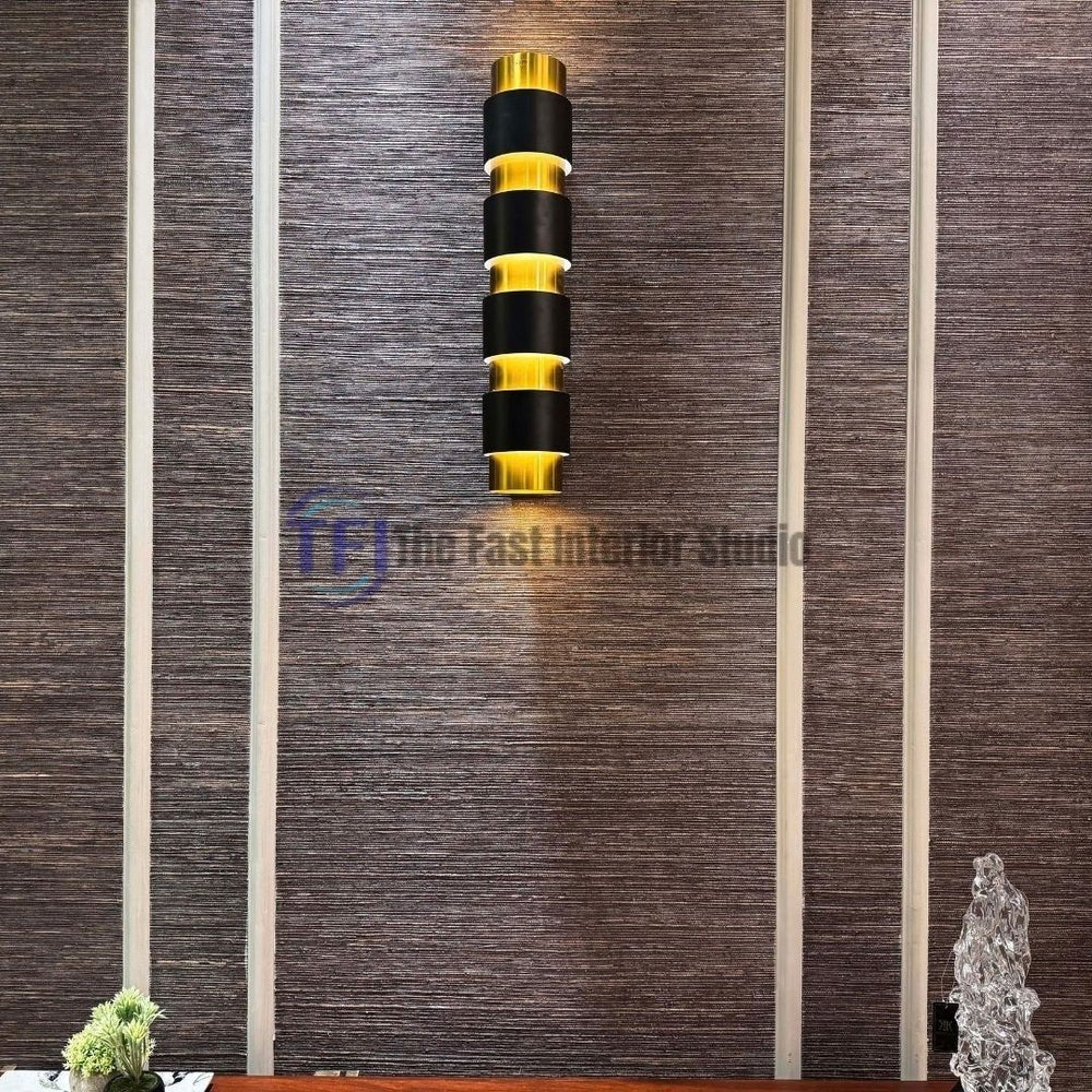 A close-up interior shot of a dark charcoal jute wallpaper installed inside white wainscoting wall paneling, featuring a modern black and gold wall sconce mounted in the center