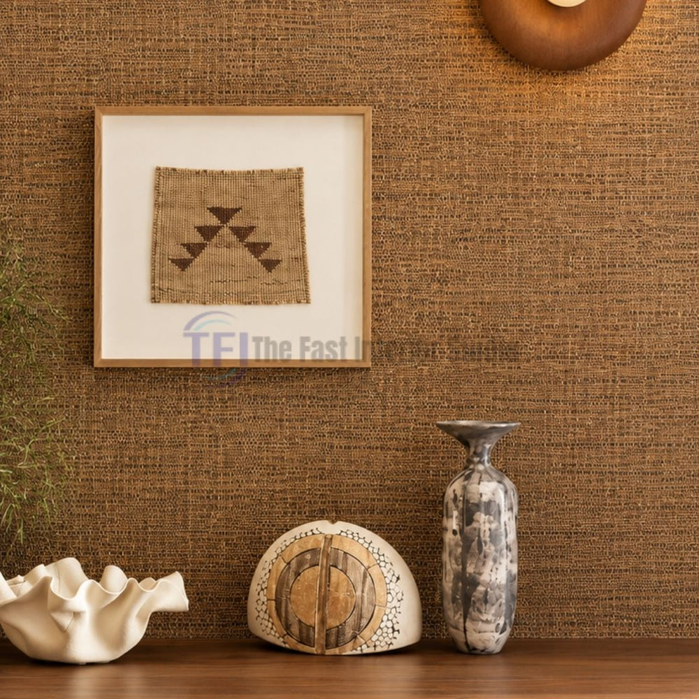 A close-up interior shot of a rich golden-brown jute wallpaper accent wall styled with a framed textile artwork, a modern wooden wall sconce, and unique ceramic sculptures on a console table