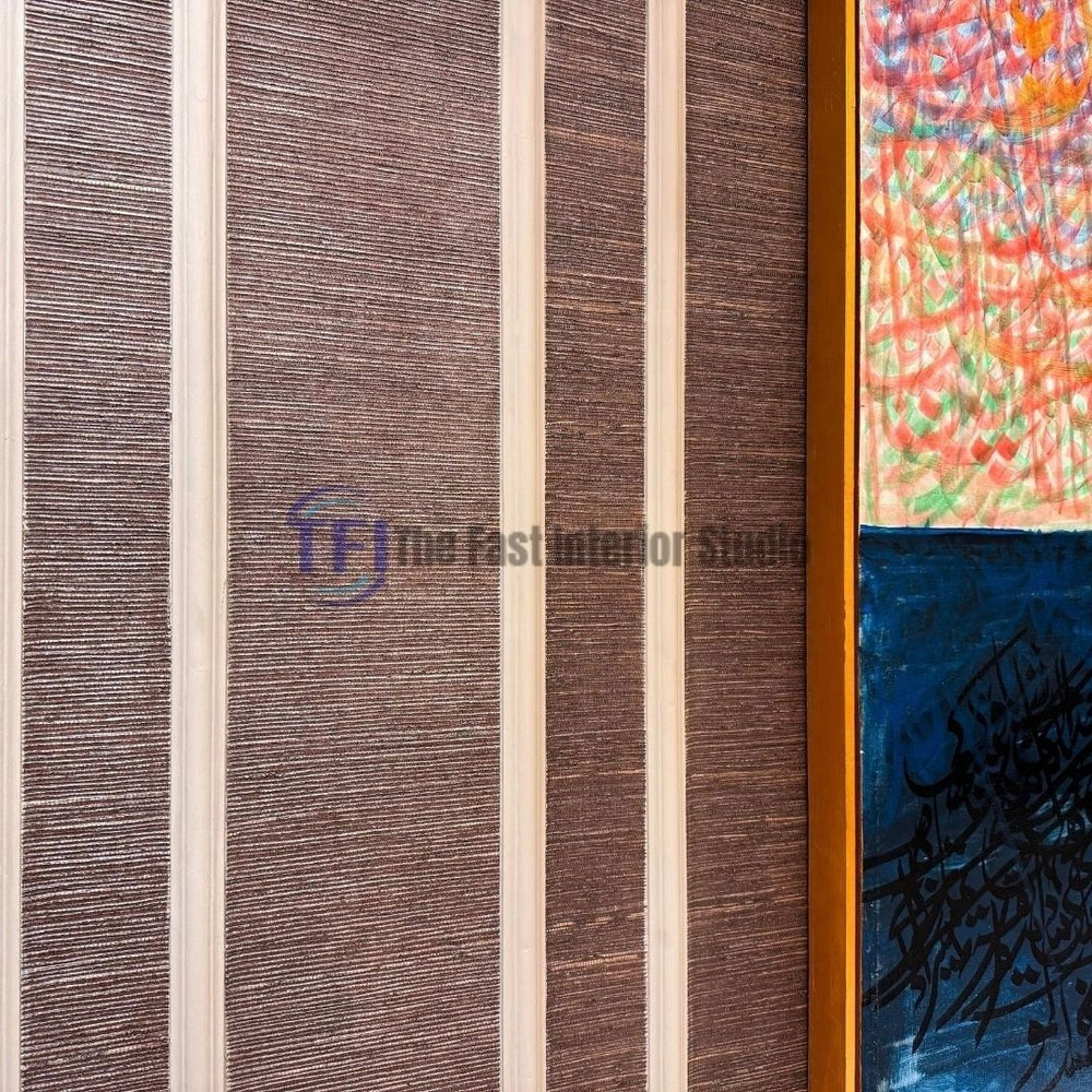 A close-up interior shot of dark brown jute wallpaper texture installed inside vertical white wainscoting wall paneling, displayed next to a framed colorful and blue calligraphic art piece