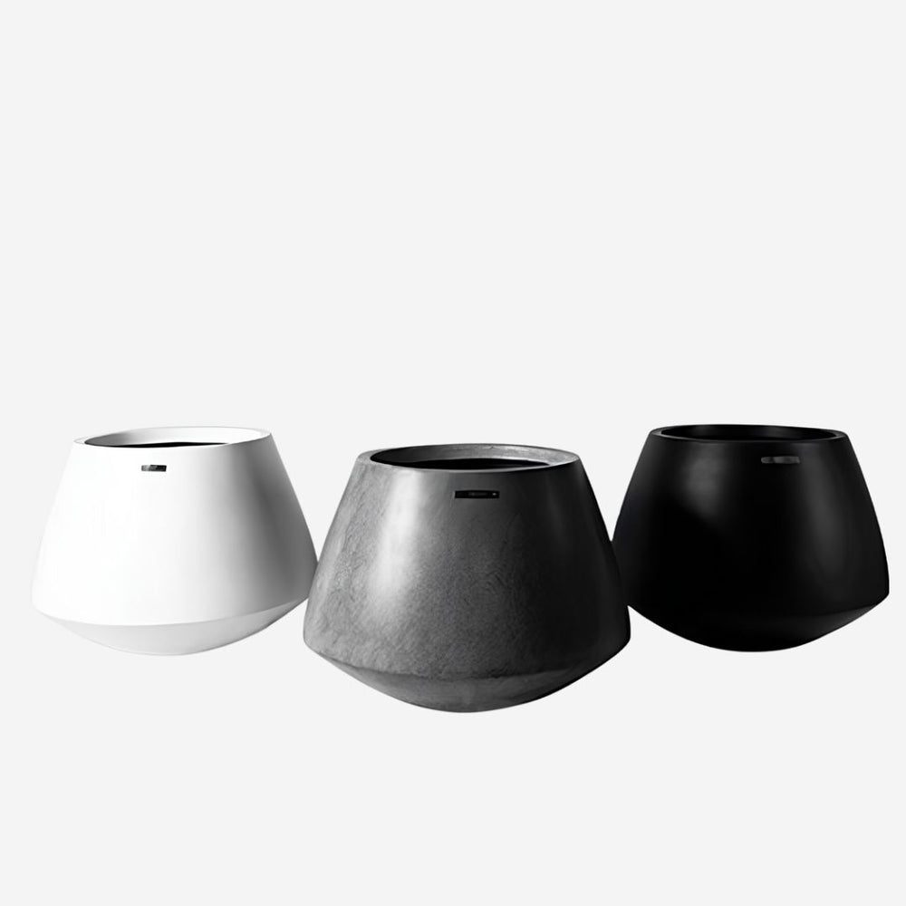A collection of three geometric faceted low-profile planters in matte white, textured stone grey, and matte black, designed for luxury indoor botanical decor