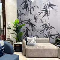 A contemporary living space showcasing a watercolor bamboo leaf mural wallpaper in black and grey tones, installed behind a taupe sectional sofa and a potted plant