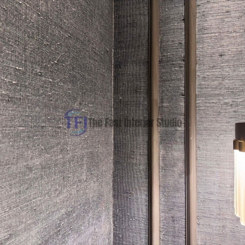 A corner interior shot of a dark charcoal jute wallpaper accent wall installed beside vertical decorative wall molding and a glowing wall sconce