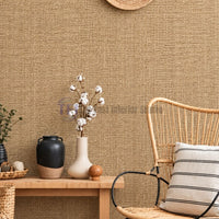 A cozy interior setting featuring a realistic textured jute weave wall covering styled behind a wooden console table, ceramic vases, and a natural rattan armchair