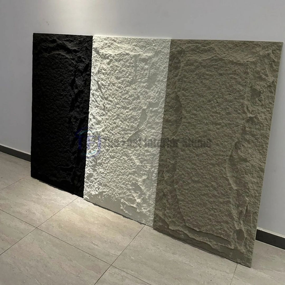 A display of three large vertical 3D PU chiseled faux stone wall panels in black, white, and warm beige, resting against a white wall in a modern setting