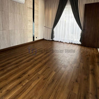 A formal living space featuring deep, rich brown Chaina Floor 12 MM wood laminate flooring, contrasting with a light textured accent wall and heavy draping curtains