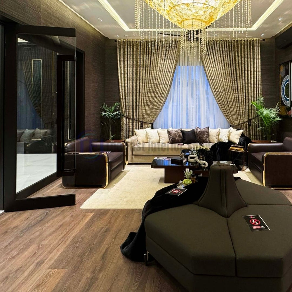A highly opulent, expansive living room interior grounded by rich, medium-brown AGT wooden laminate flooring, featuring dark leather sofas, textured walls, and a grand crystal chandelier