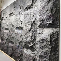 A large feature wall cladded with interlocking dark charcoal 3D PU faux stone panels, showcasing deep, realistic cliff rock textures under accent lighting