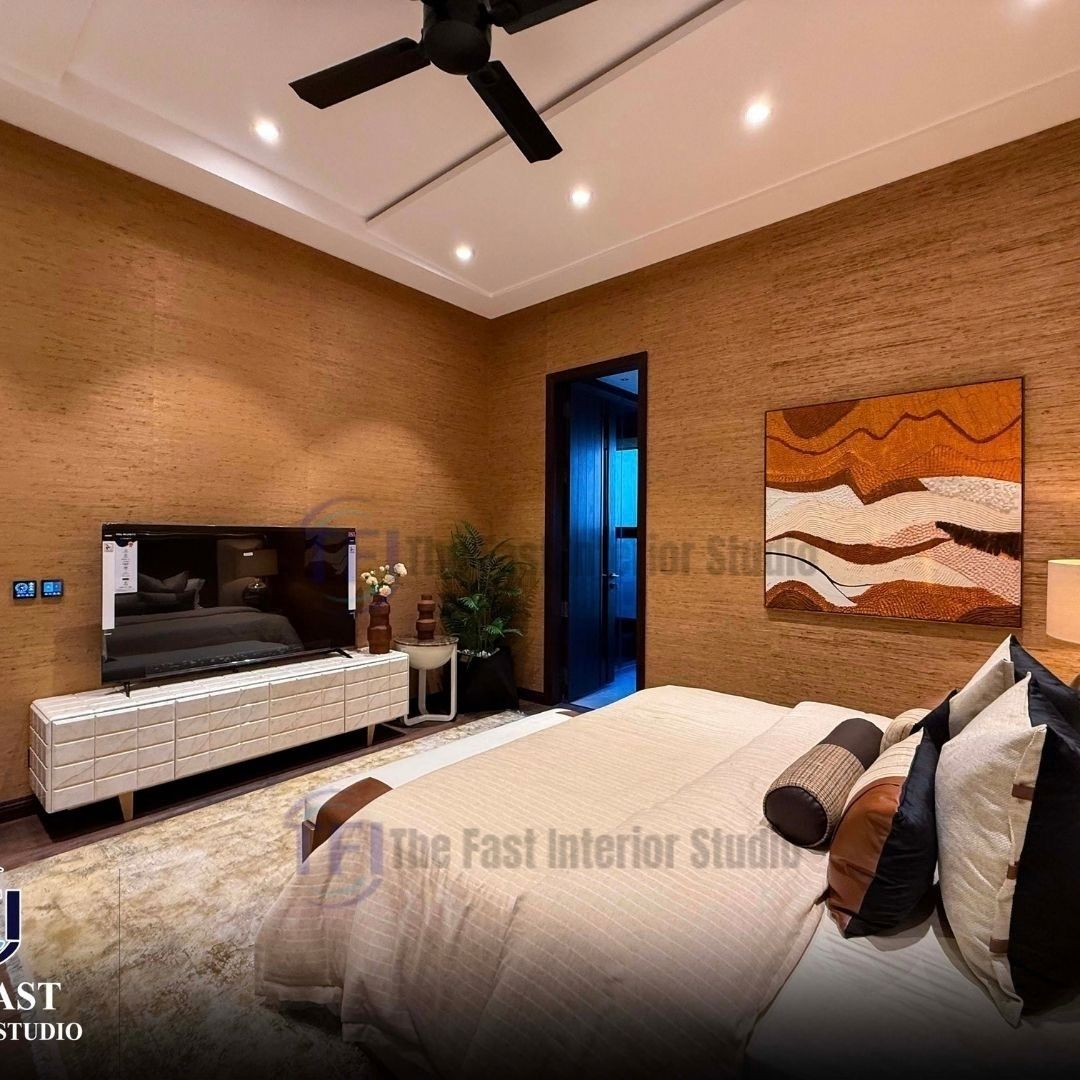 A luxurious bedroom interior featuring natural golden-brown jute wallpaper installed across full walls, styled with a white media console, a television, and abstract earth-toned wall art