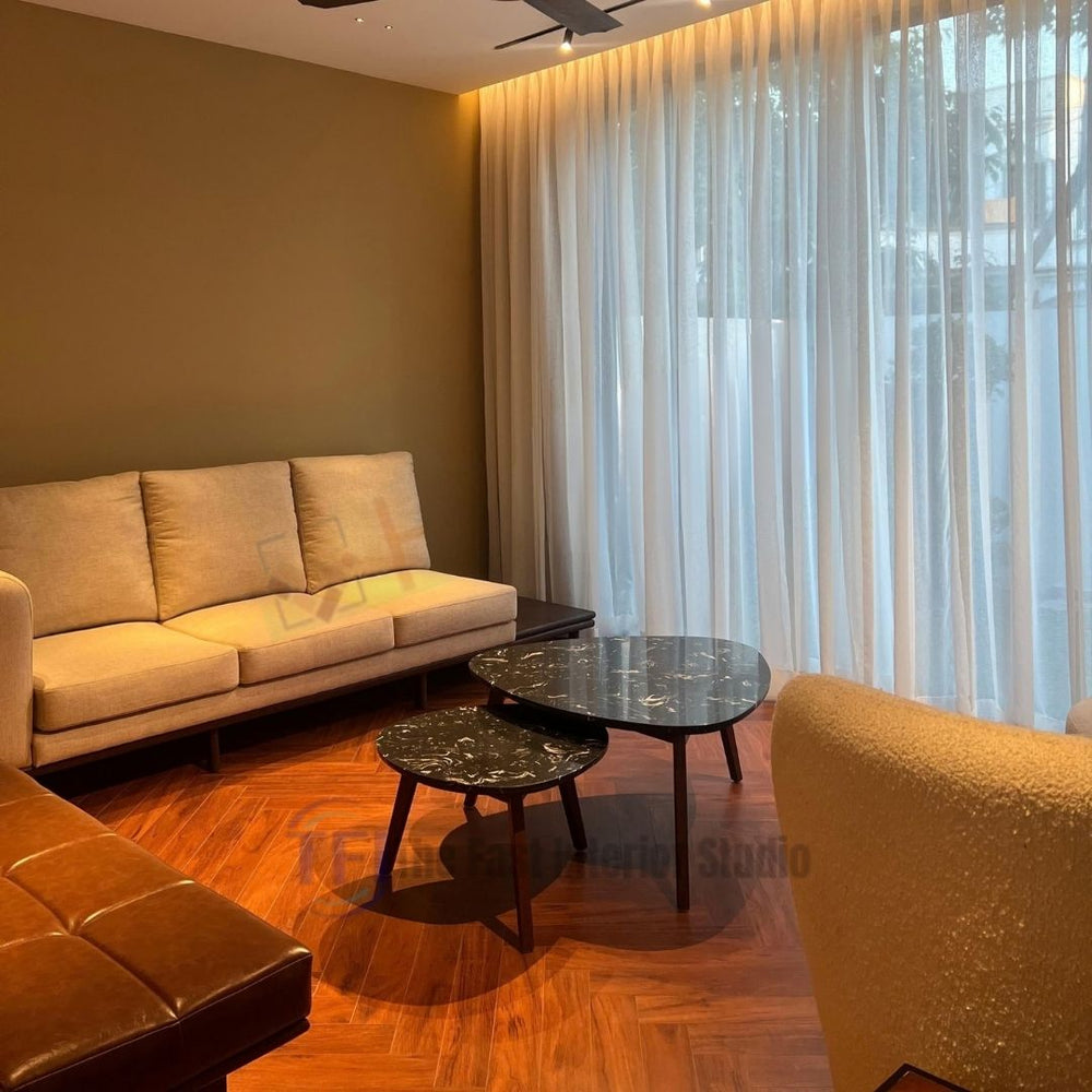 A luxurious living room featuring the best wooden flooring in Pakistan, showcasing Chaina Floor 12 MM medium brown herringbone laminate next to a cream sofa and black marble nested tables