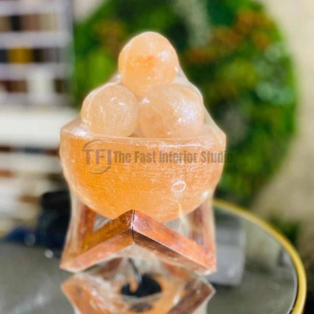 A luxury Himalayan salt lamp featuring a hand-carved salt bowl filled with glowing pink salt spheres, resting on a crossed wooden base