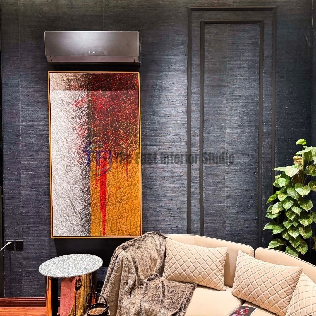 A modern living room interior featuring deep navy blue jute wallpaper installed behind a cream quilted sofa, a large vertical abstract art piece, and a small side table