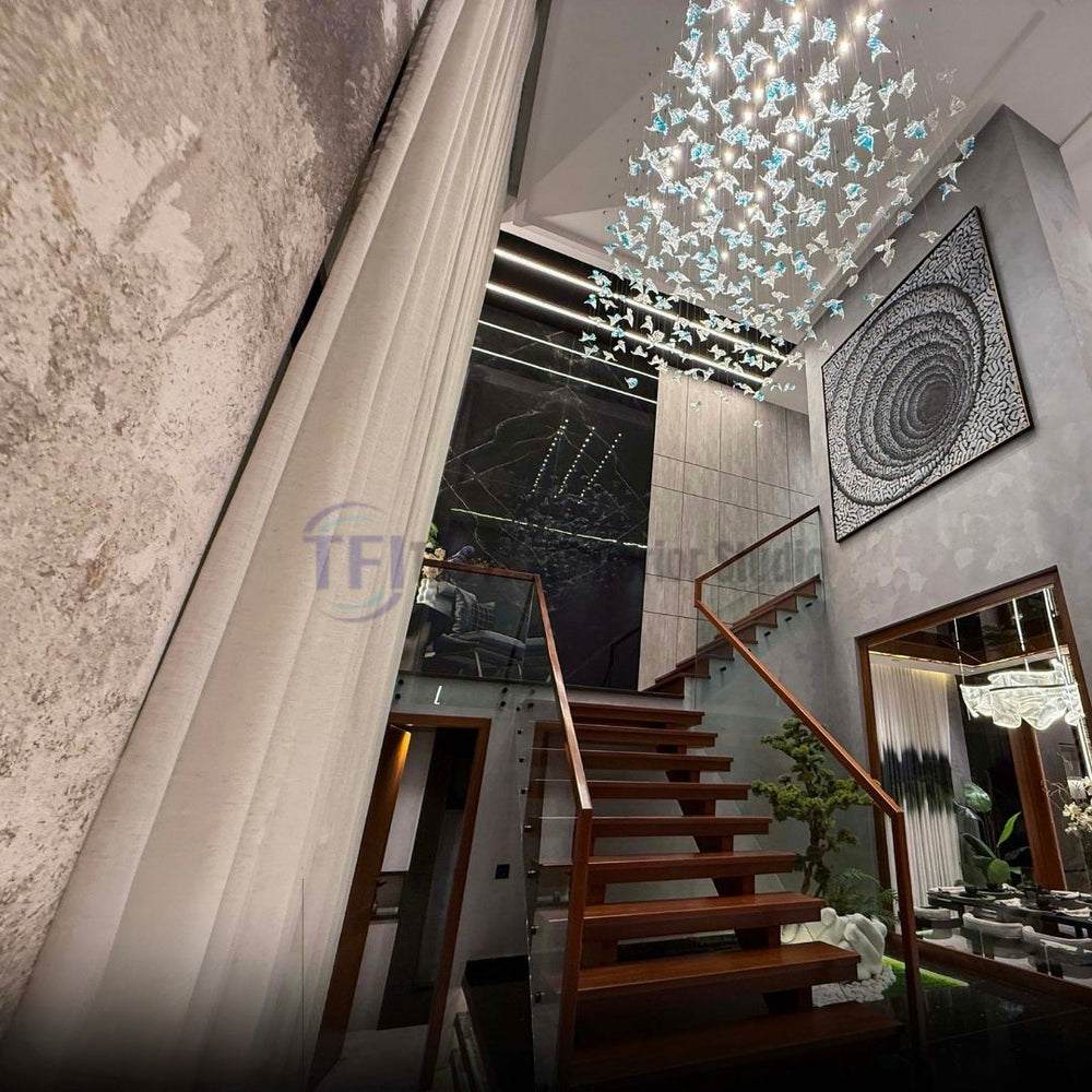 A modern multi-level home entrance showcasing tall pleated curtains draping down next to wooden stairs, styled with a geometric canvas art piece and elaborate ceiling lighting