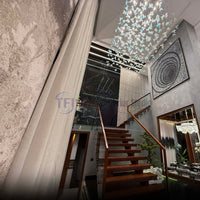 A modern multi-level home entrance showcasing tall pleated curtains draping down next to wooden stairs, styled with a geometric canvas art piece and elaborate ceiling lighting