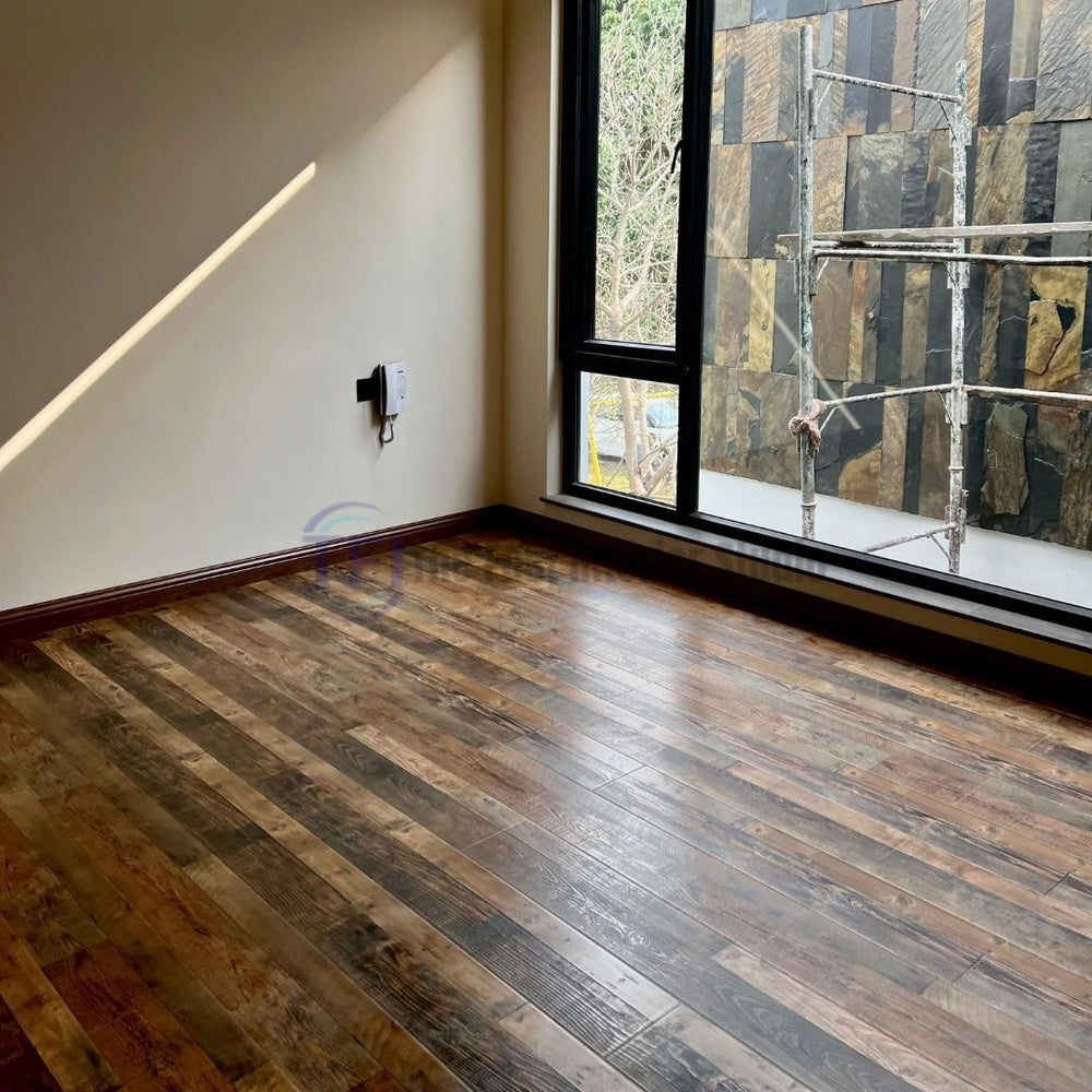 A modern room with large windows overlooking a stone wall, grounded by premium Chaina Floor 12 MM laminate in a striking multi-tone rustic finish