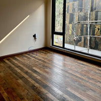 A modern room with large windows overlooking a stone wall, grounded by premium Chaina Floor 12 MM laminate in a striking multi-tone rustic finish