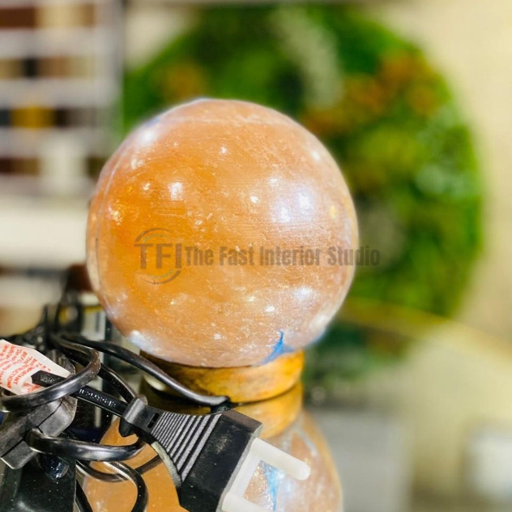 A polished spherical Himalayan salt globe lamp emitting a warm amber glow, resting on a small round wooden base