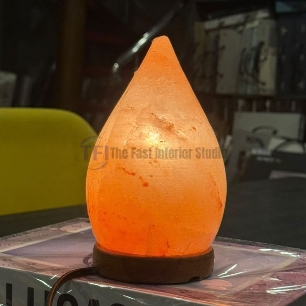 A premium teardrop-shaped Himalayan salt lamp emitting a warm amber glow, resting on a round wooden base and styled as luxury ambient decor