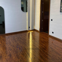 A pristine installation of high-gloss rosewood Chaina Floor 12 MM laminate flooring, featuring matching wooden baseboards and transitioning into a dark tiled hallway