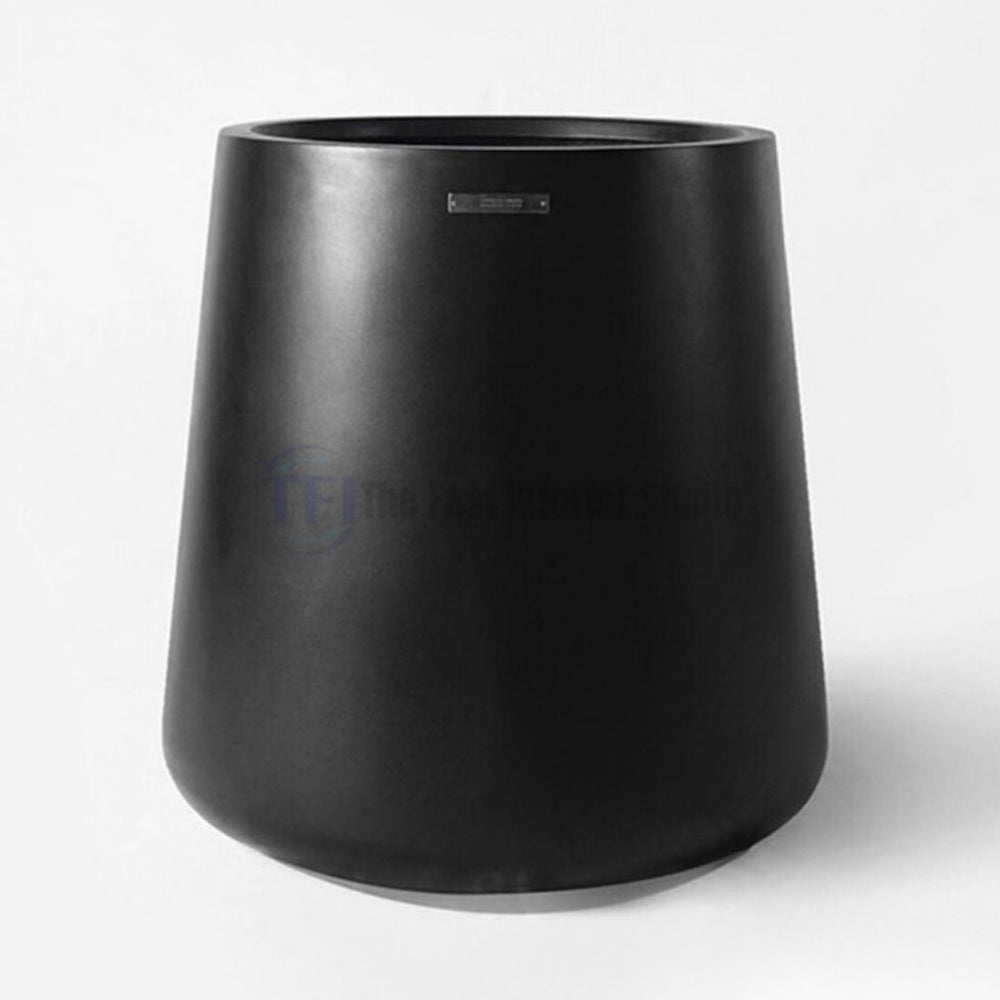 A sleek, modern matte black tapered plant pot featuring a small metallic badge, designed for luxury indoor botanical decor in Lahore