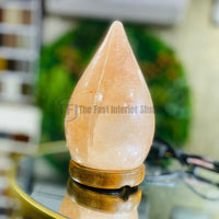 A smooth teardrop-shaped Himalayan salt lamp emitting a warm amber glow, resting on a round wooden base