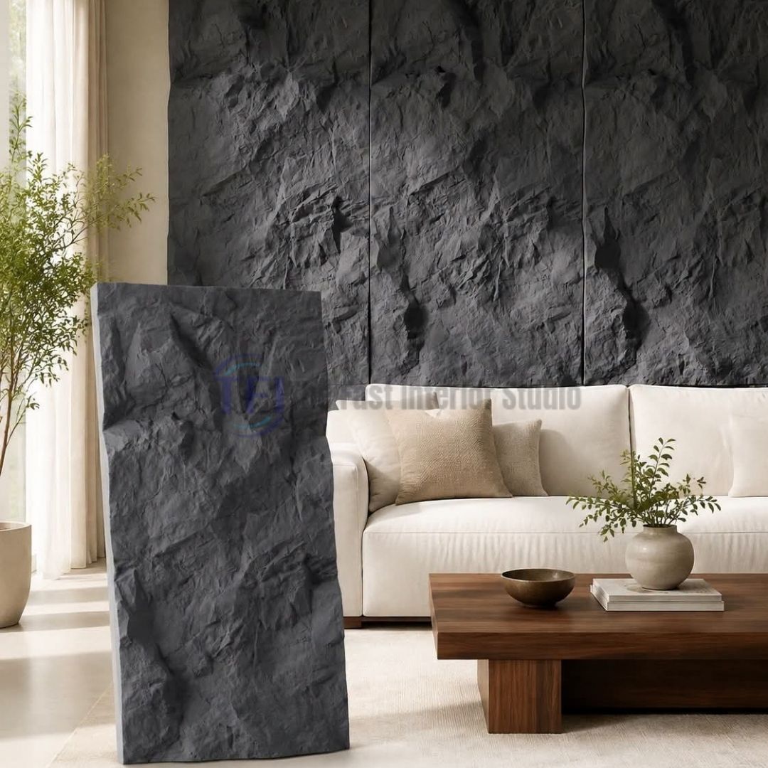 A standalone sample of a dark grey 3D PU chiseled faux stone panel displayed in front of a matching expansive feature wall, styled behind a cream sofa in a modern luxury living room