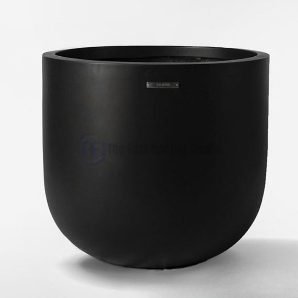 A top-ranking premium matte black plant pot featuring a sleek cylindrical body with a smooth rounded base and a small metallic badge, styled for luxury indoor decor in Pakistan