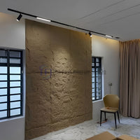 A warm tan large block 3D PU faux stone accent wall installed between two windows, highlighted by modern black ceiling track lighting