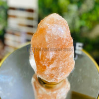An authentic natural raw rock Himalayan salt lamp with a rugged unrefined texture, emitting a warm amber glow on a minimalist base