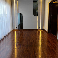 An empty room showcasing the striking reflective surface of Chaina Floor 12 MM high-gloss dark wood laminate, mirroring the modern wall lighting