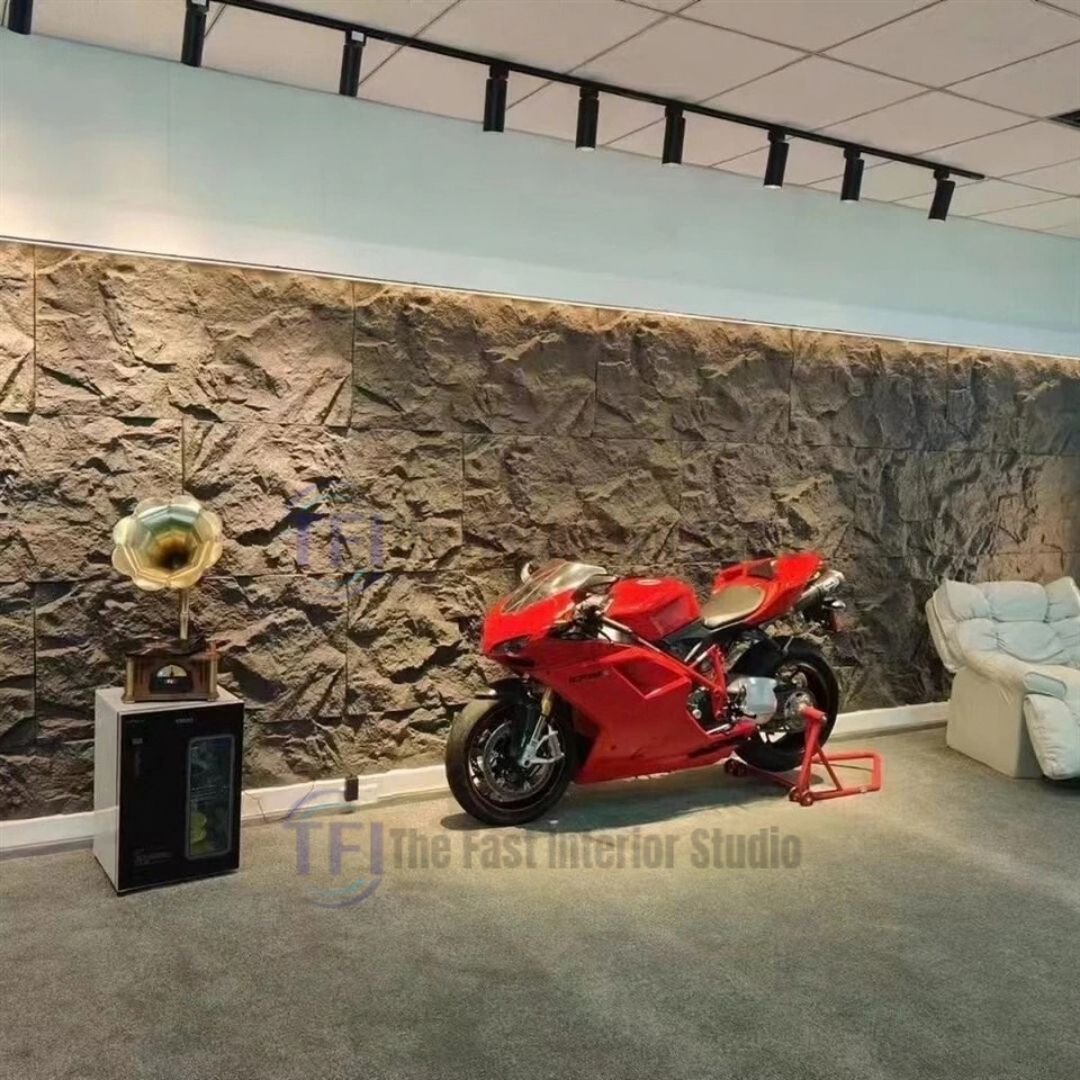 An expansive commercial showroom featuring a massive dark grey 3D PU cliff rock feature wall, styled as a dramatic backdrop for a red sports motorcycle and luxury seating