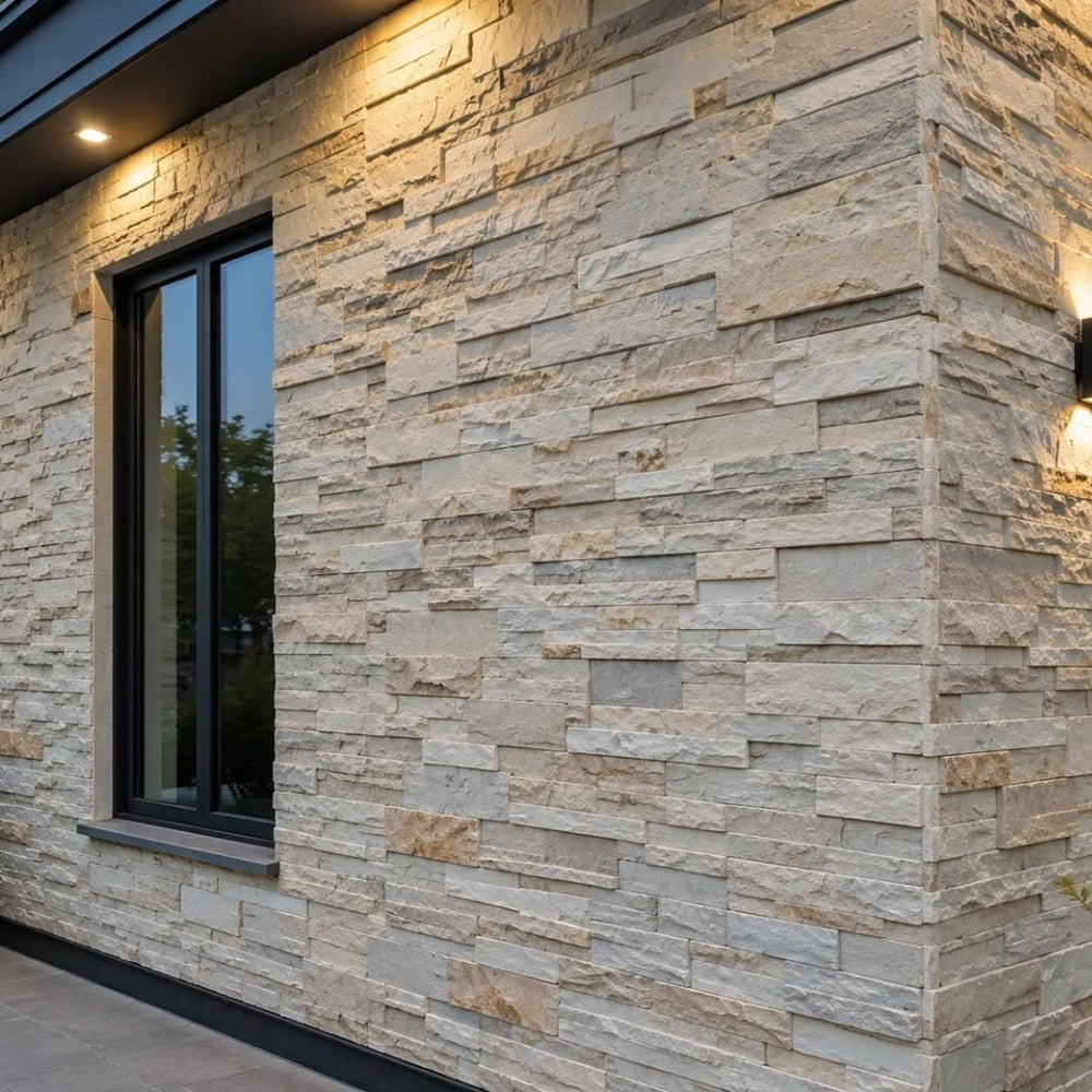 An exterior property wall cladded with light beige 3D PU stacked faux stone panels, beautifully illuminated by modern architectural sconce lighting