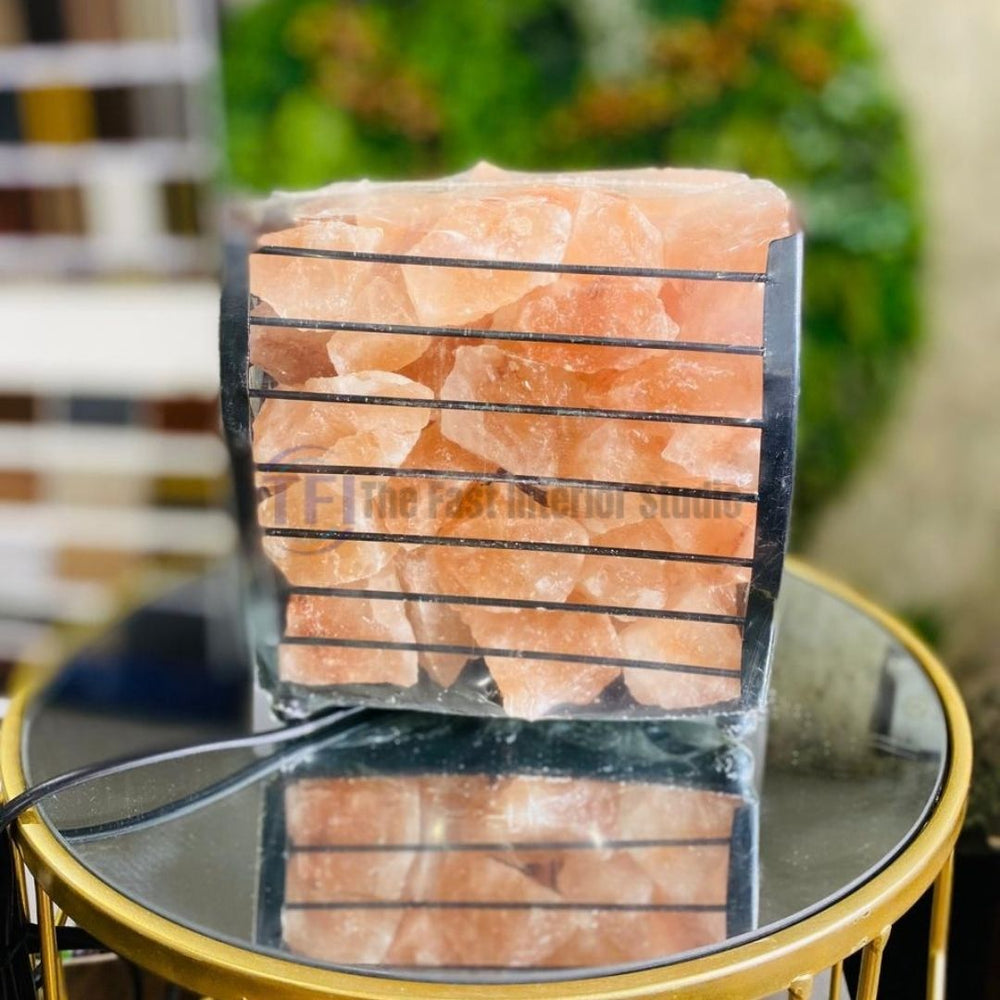 An industrial-chic Himalayan salt lamp featuring natural salt chunks housed inside a square black metal wire basket