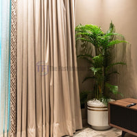 Beige curtains with geometric trim and blue sheers beside a potted palm
