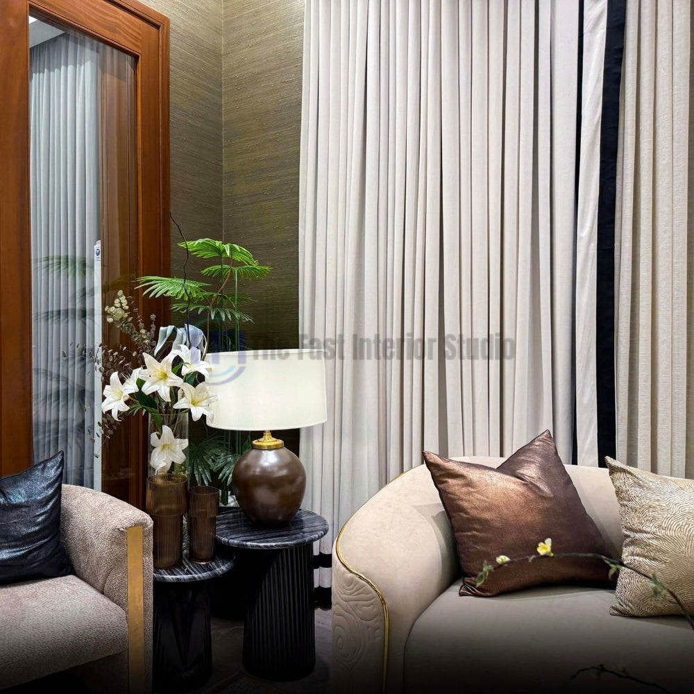 Close-up of pleated beige curtains with black edge trim next to a curved sofa and side table