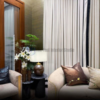 Close-up of pleated beige curtains with black edge trim next to a curved sofa and side table