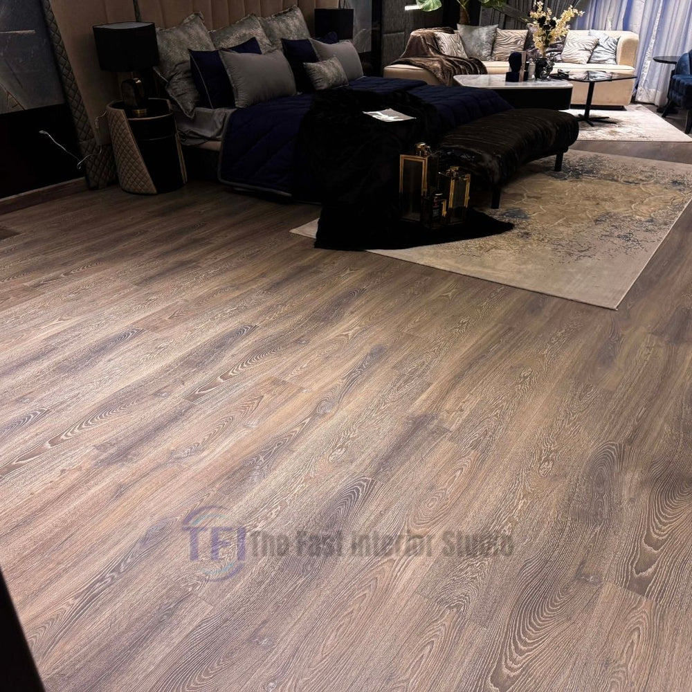 Close-up of premium taupe wood laminate flooring with authentic sweeping grain lines, installed seamlessly next to a dark velvet bench