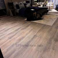 Close-up of premium taupe wood laminate flooring with authentic sweeping grain lines, installed seamlessly next to a dark velvet bench