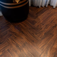 Close-up view of rich dark wood AGT laminate flooring laid in a classic herringbone geometric pattern, highlighting the authentic wood grain and seamless plank joints