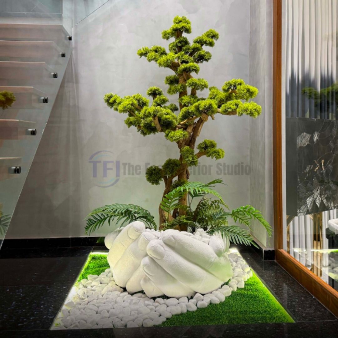 Custom 6-foot artificial bonsai tree in a white sculpted hand pot surrounded by white stones near a modern staircase
