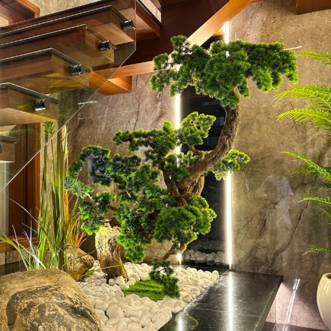 Custom artificial bonsai tree installed in a white stone indoor garden beneath a modern wood and glass staircase