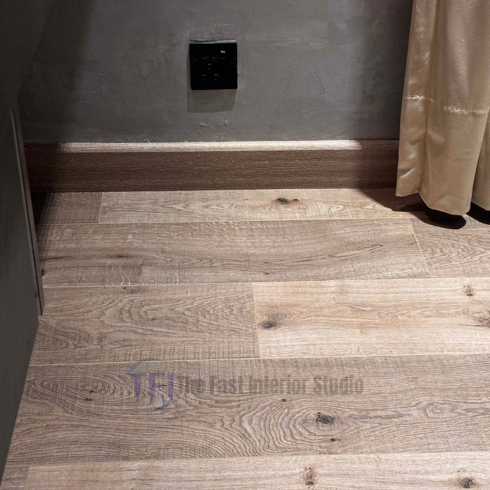 Detailed close-up of light knotted oak laminate planks installed flawlessly against a matching architectural wood-tone baseboard