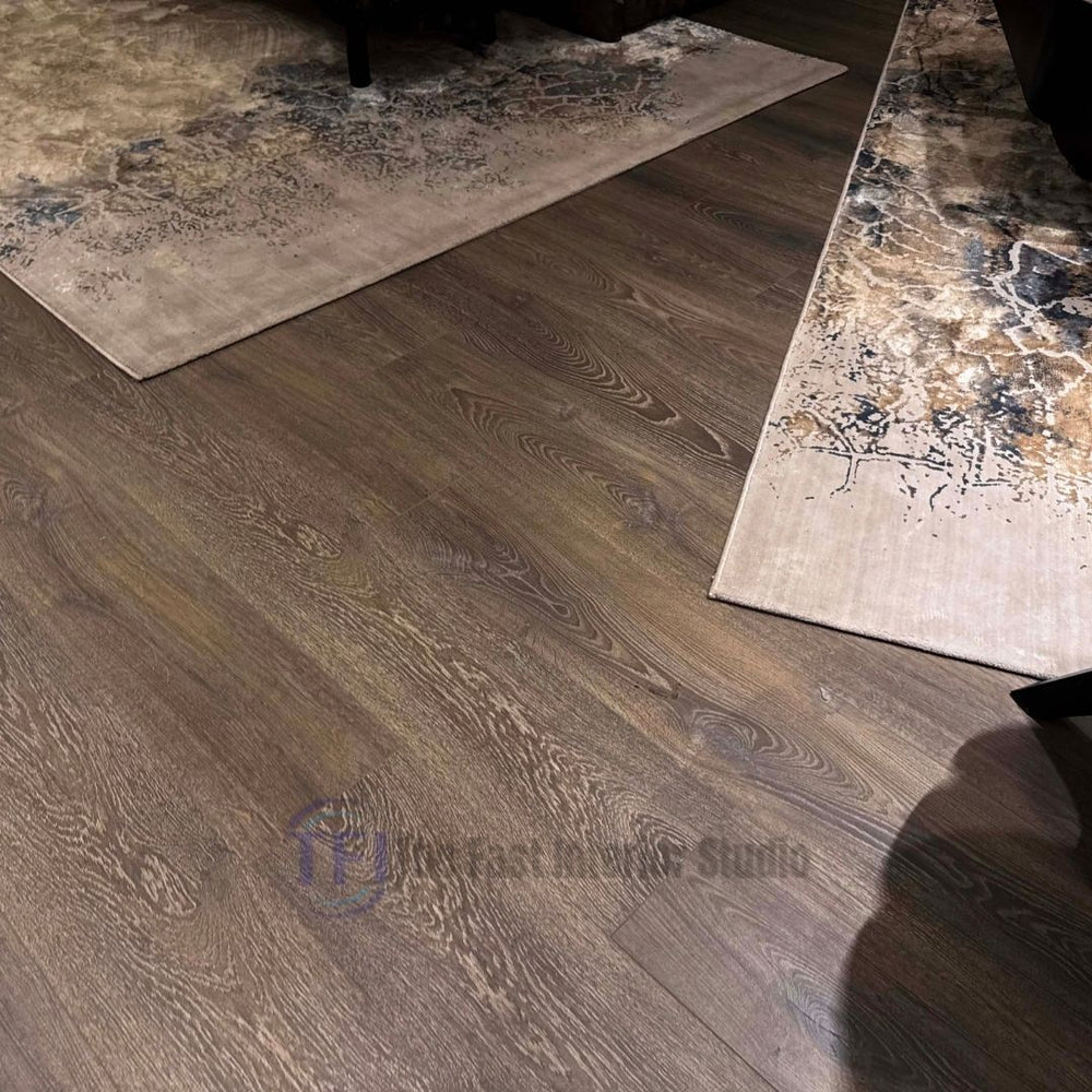 Detailed view of textured grey-brown wood laminate flooring with distinct grain patterns, positioned perfectly between two overlapping patterned rugs
