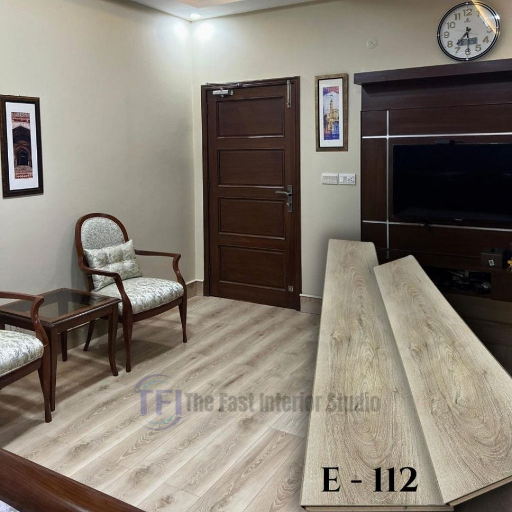 Light oak wood laminate flooring model E-112 shown both as loose interlocking planks in the foreground and fully installed in a classic room setting featuring a dark wooden door, a dark media console, and traditional seating