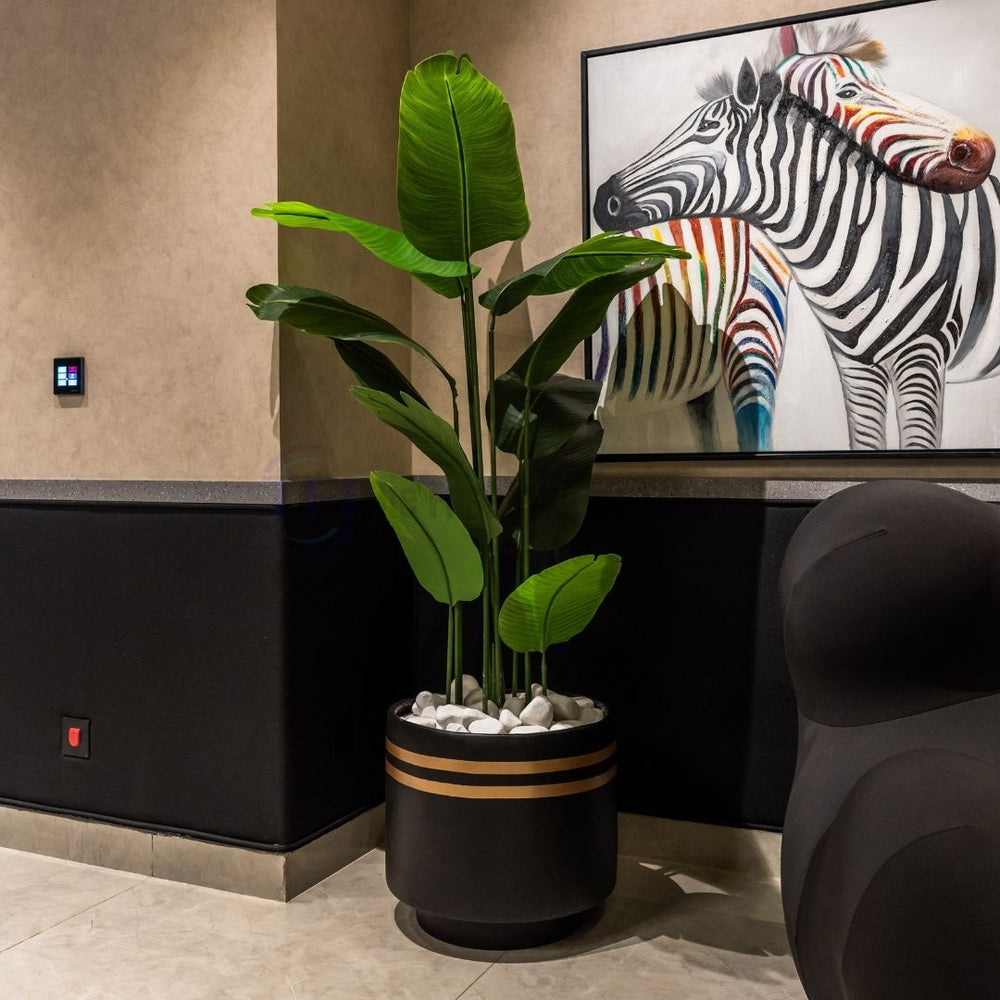 Luxury artificial indoor plant in a black and gold striped pot placed in a modern room with a black accent chair