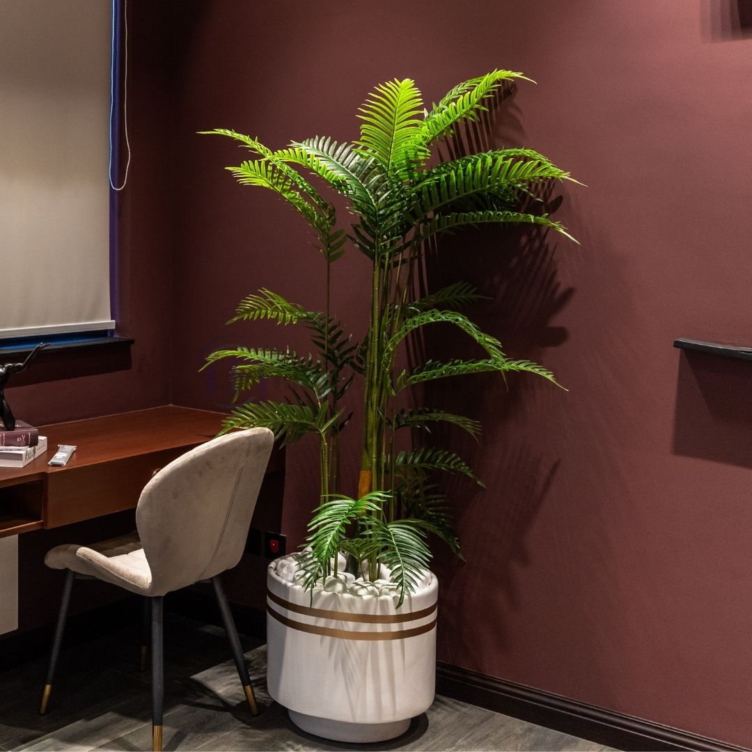 Luxury artificial indoor plant in a white pot with gold stripes placed beside a desk in a room with burgundy walls