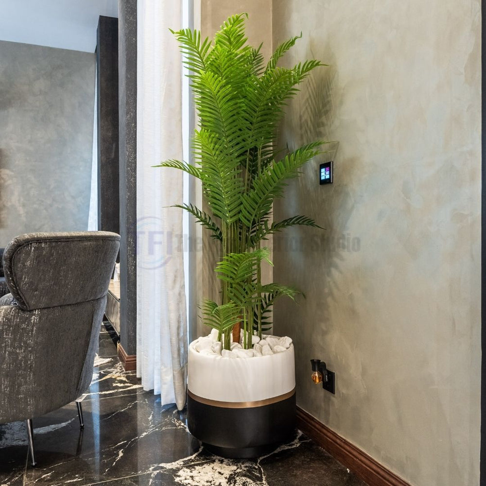 Tall 6-foot artificial palm plant in a two-tone white and black pot filled with white stones on a black marble floor