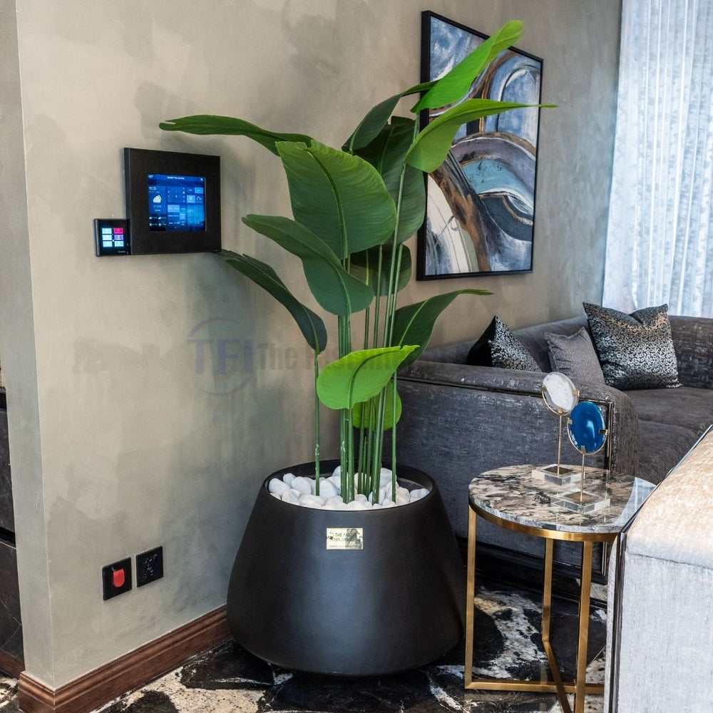 Tall 6-foot artificial plant with broad green leaves in a matte black pot filled with white stones