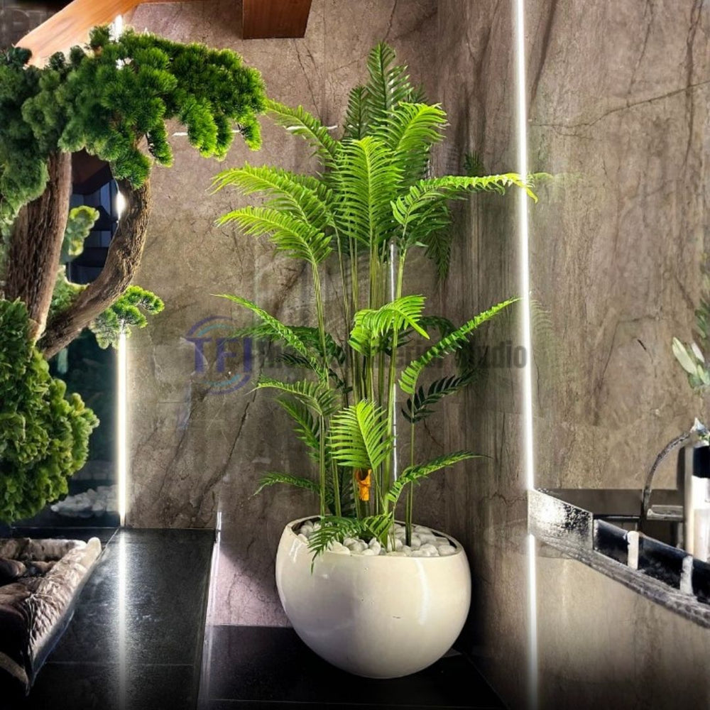 Tall artificial fern plant in a modern rounded white pot filled with white stones against a marble wall