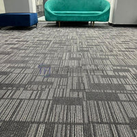 Textured charcoal grey carpet tiles installed in a modern lounge area featuring a vibrant green sofa in Lahore